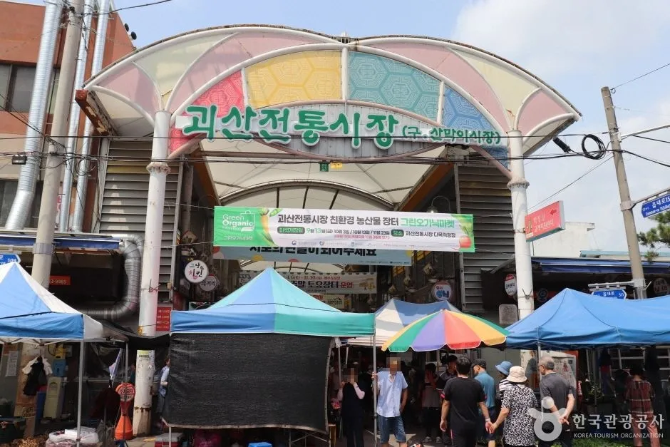 파라솔 좌판과 천막이 펼쳐진 괴산전통시장(구 산막이시장) 입구 아치